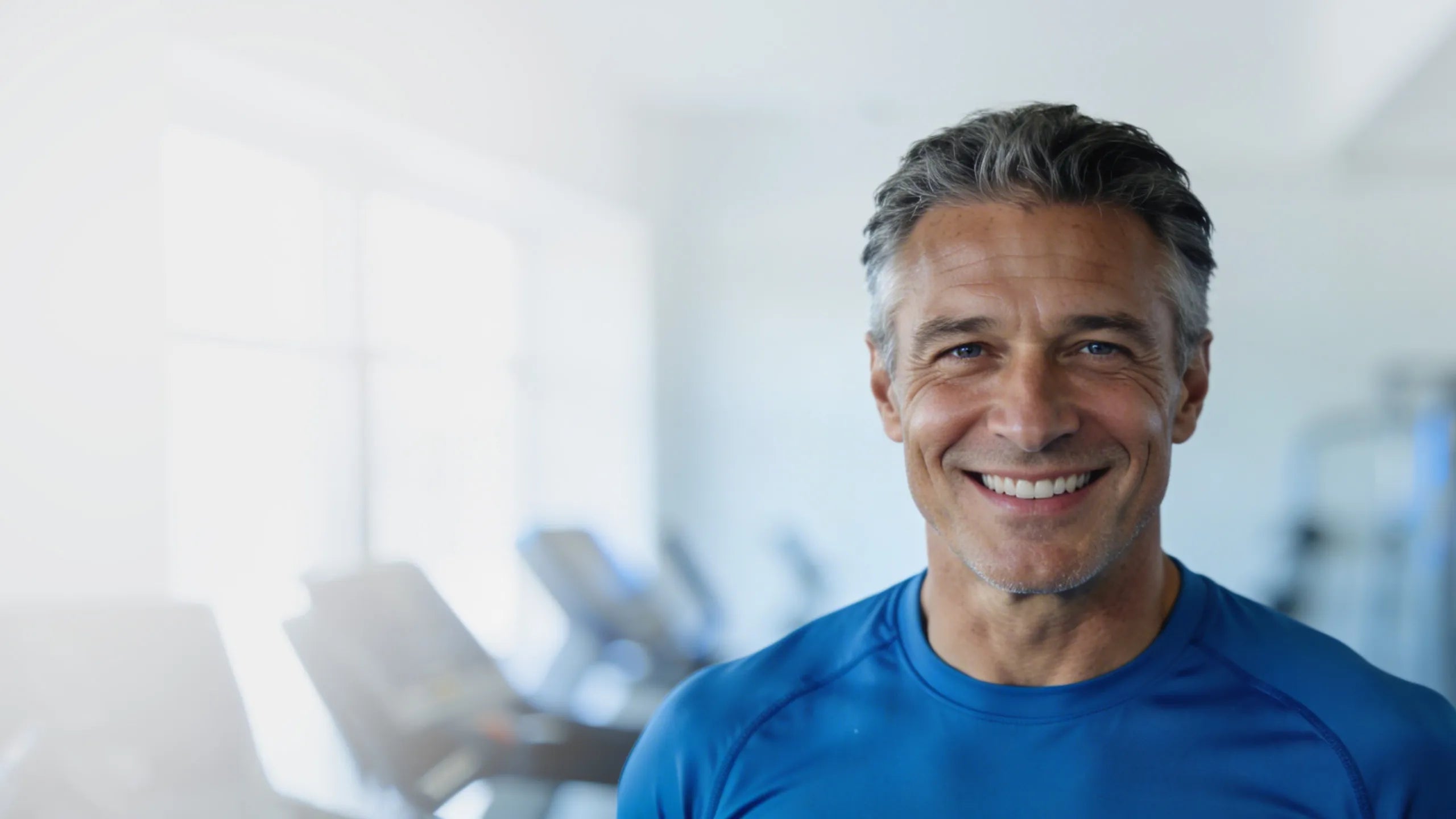 A man in a blue athletic shirt standing in a bright gym, with his face obscured.
